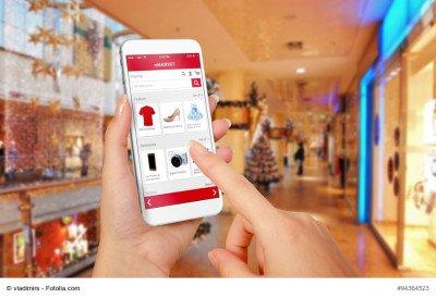 Smart phone online shopping in woman hand during Christmas. Shopping center in background. Buy clothes shoes accessories with e commerce web site