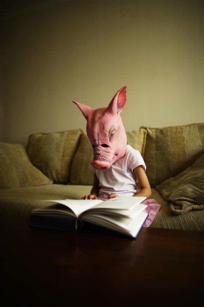 Girl in pig mask reads book Potbox.it