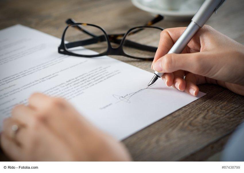 Closeup shot of a woman signing a form. She's writing on a financial contract. Shallow depth of field with focus on tip of the pen.