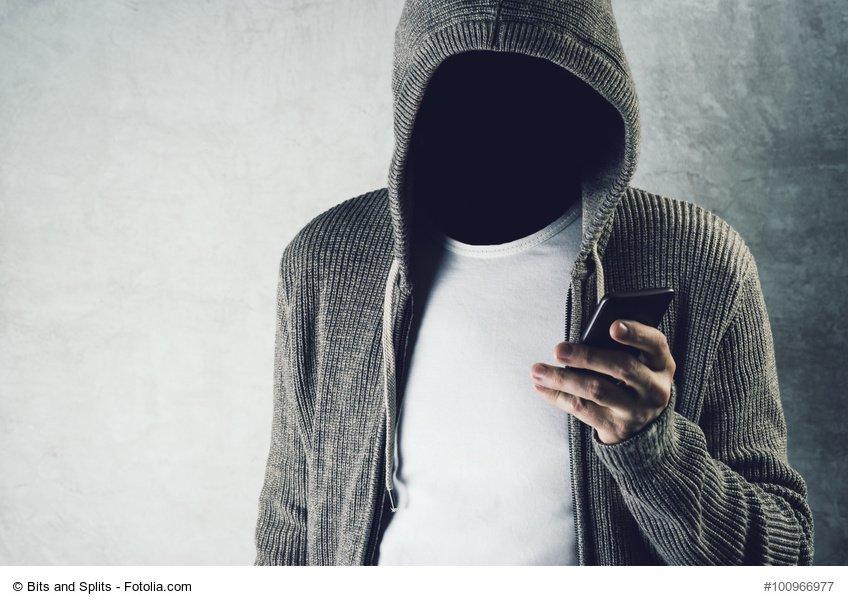 Faceless hooded person using mobile phone, identity theft concep