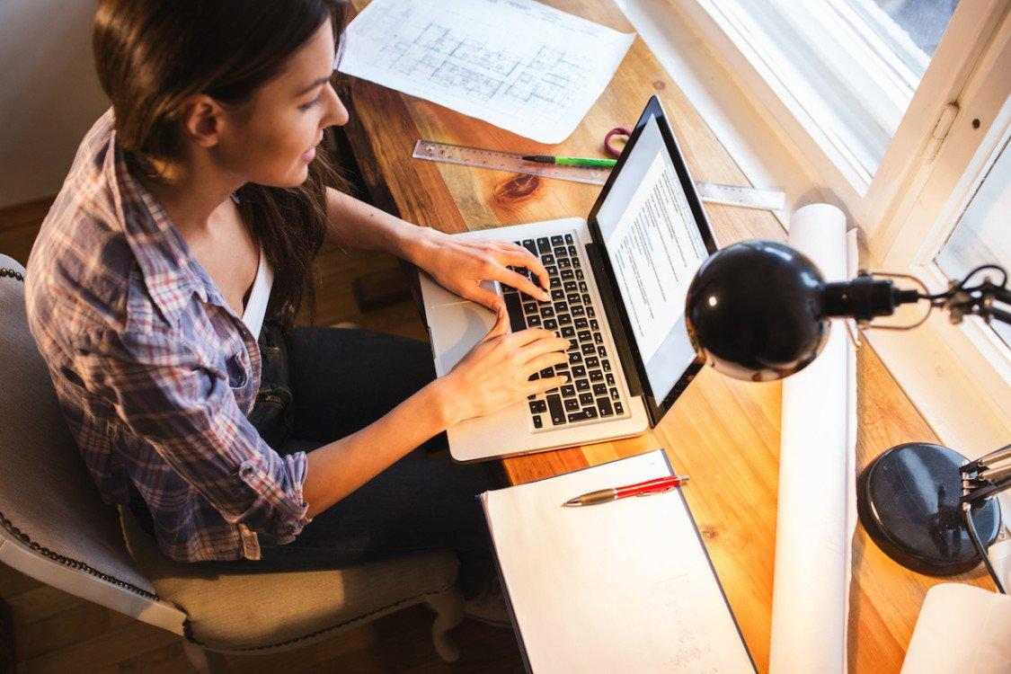 Young female student working at home.She sitting in her working room and typing something on laptop.