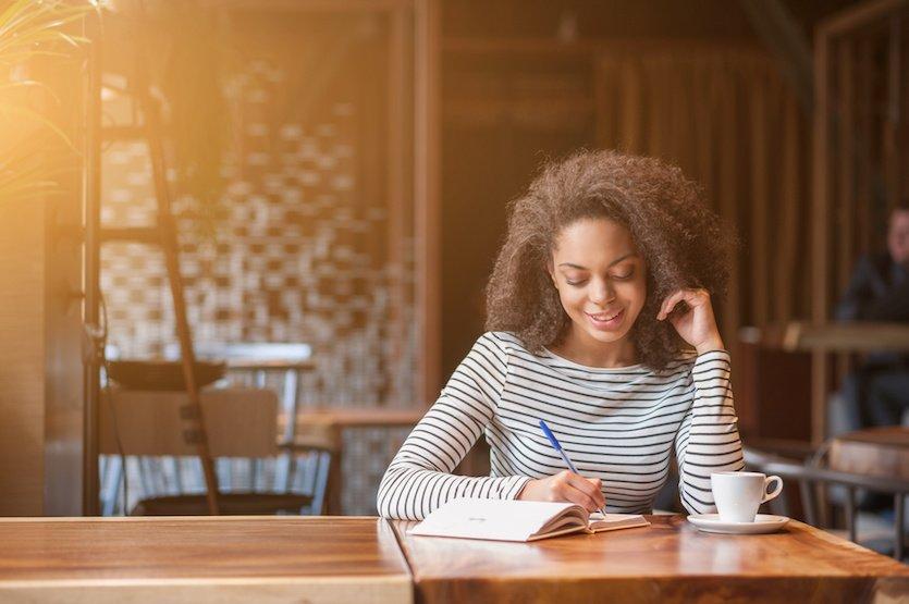 Attractive african girl is studying in cafeteria. She is making notes and smiling