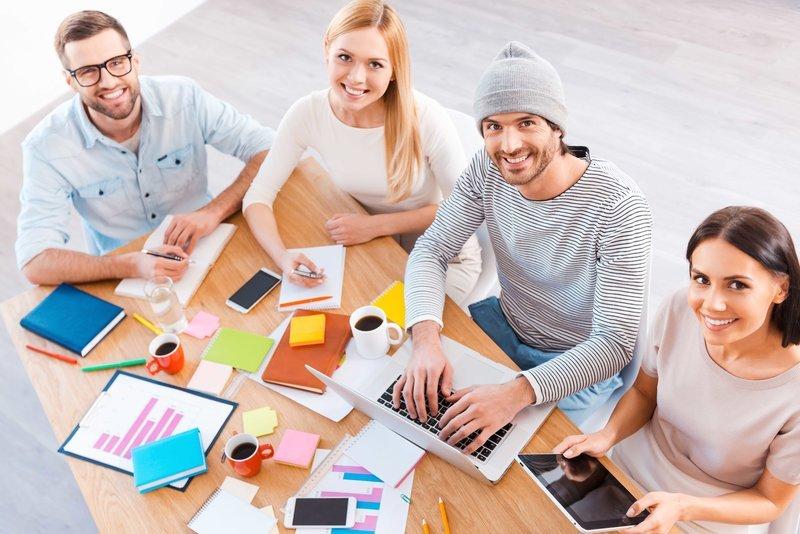 Top view of group of business people in smart casual wear working together and smiling while sitting at the wooden desk