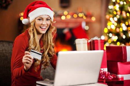 Cheerful young woman wearing Santa's hat is buying Christmas presents online.